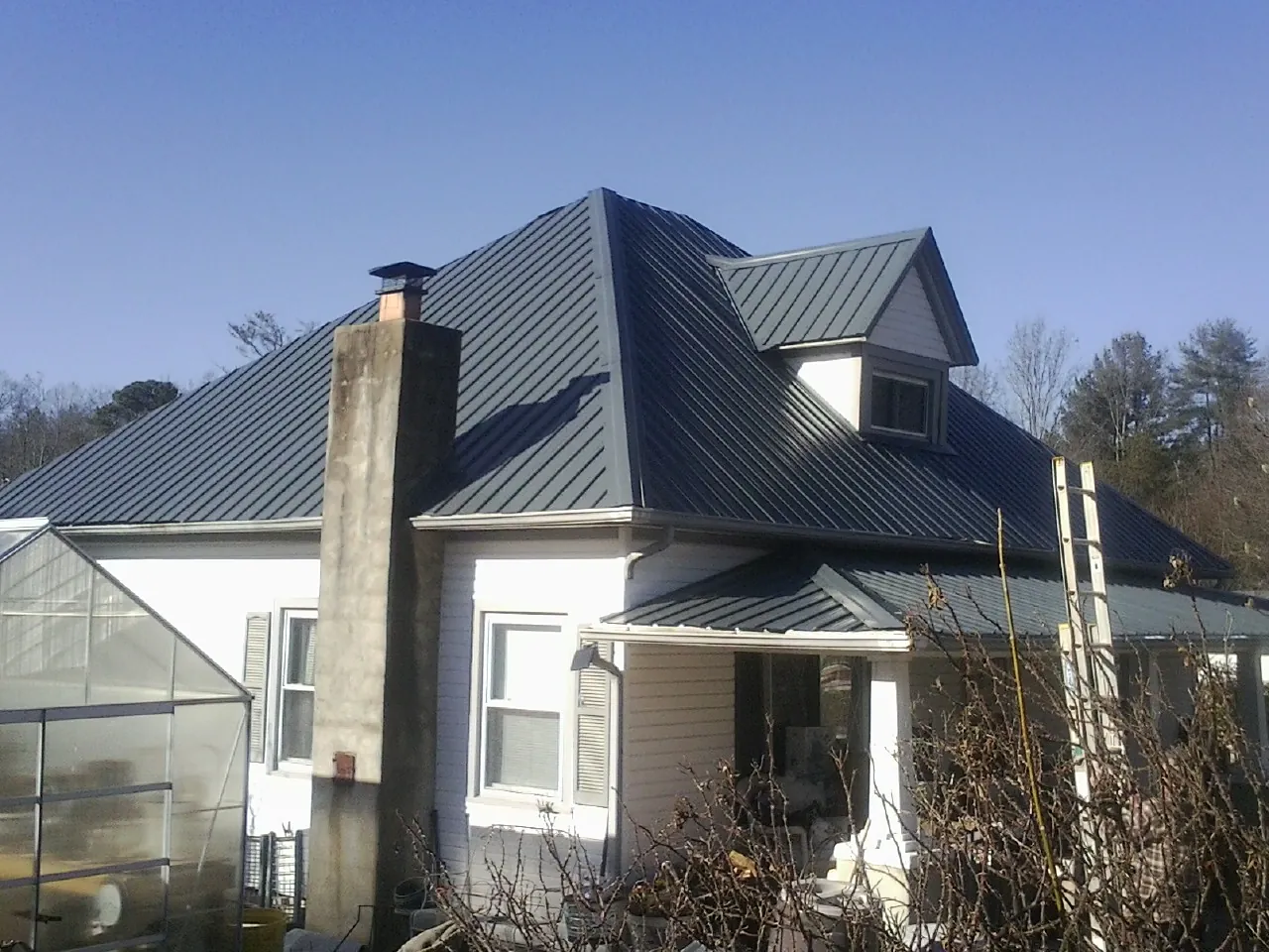 Dark blue standing seam metal roof on a white farmhouse with dormer — Slate & Tile Roof Repair by Roofing Brothers in Mapleville