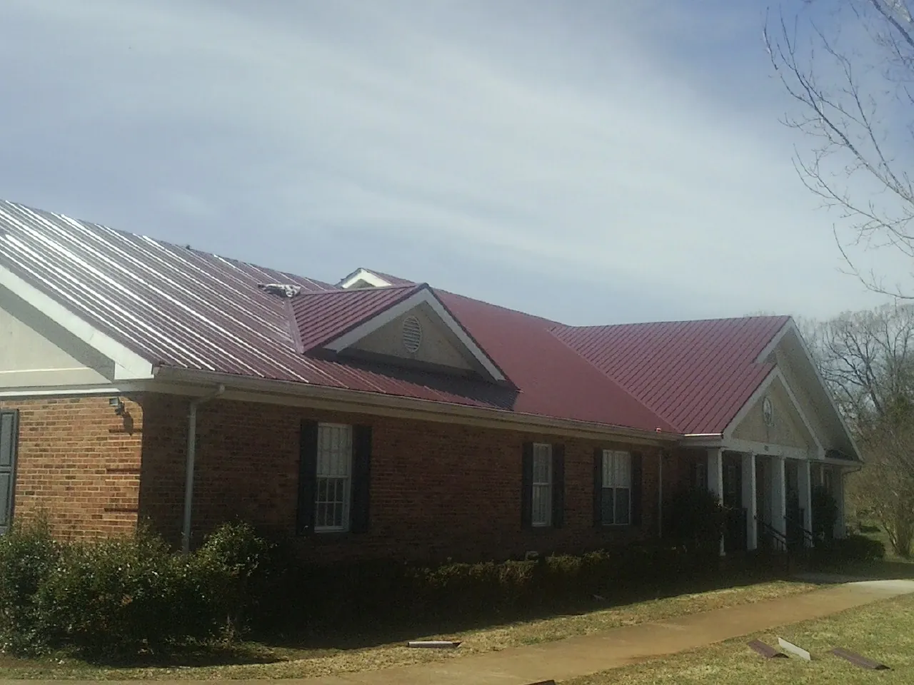 Red metal roof with gabled entries on a long brick building, from a Hail Damage Roof Repair job in Mapleville