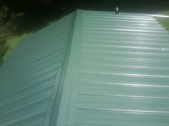 New green metal panels meeting at the ridge of a roof — Flat Roof Repair work by our crew in Mapleville
