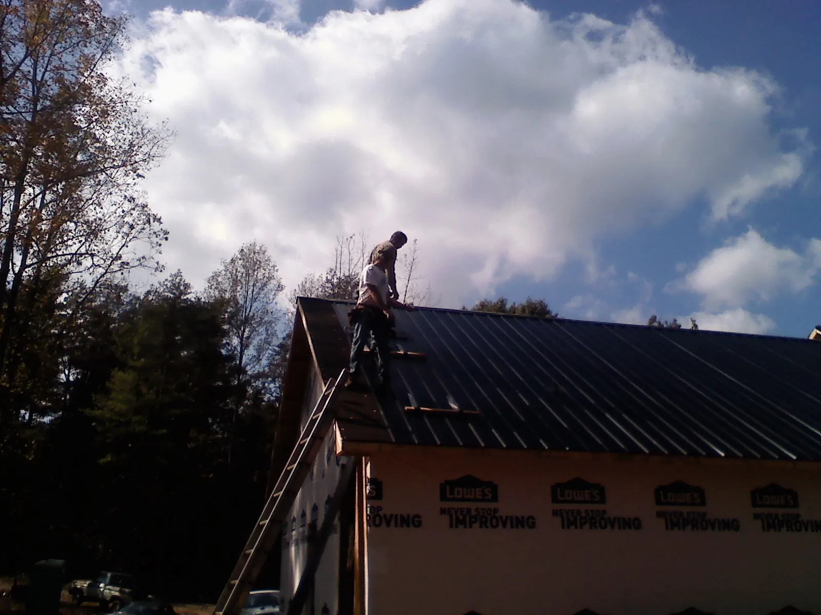 Roofer fastening dark metal panels high against a cloudy sky, from a Roof Inspection job in Mapleville