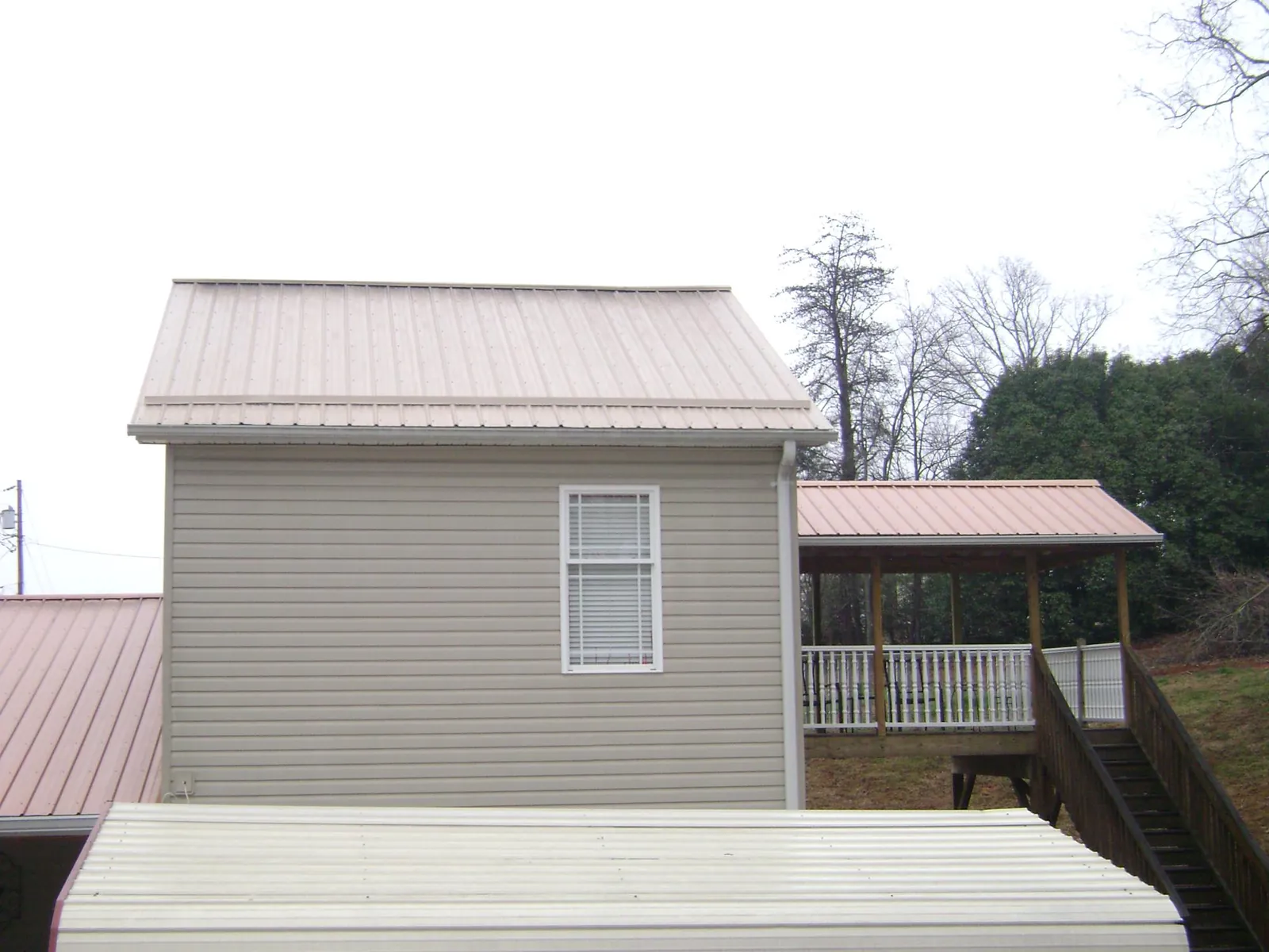 Tan metal roofs on a two story addition and attached porch, from a Roof Replacement job in Mapleville